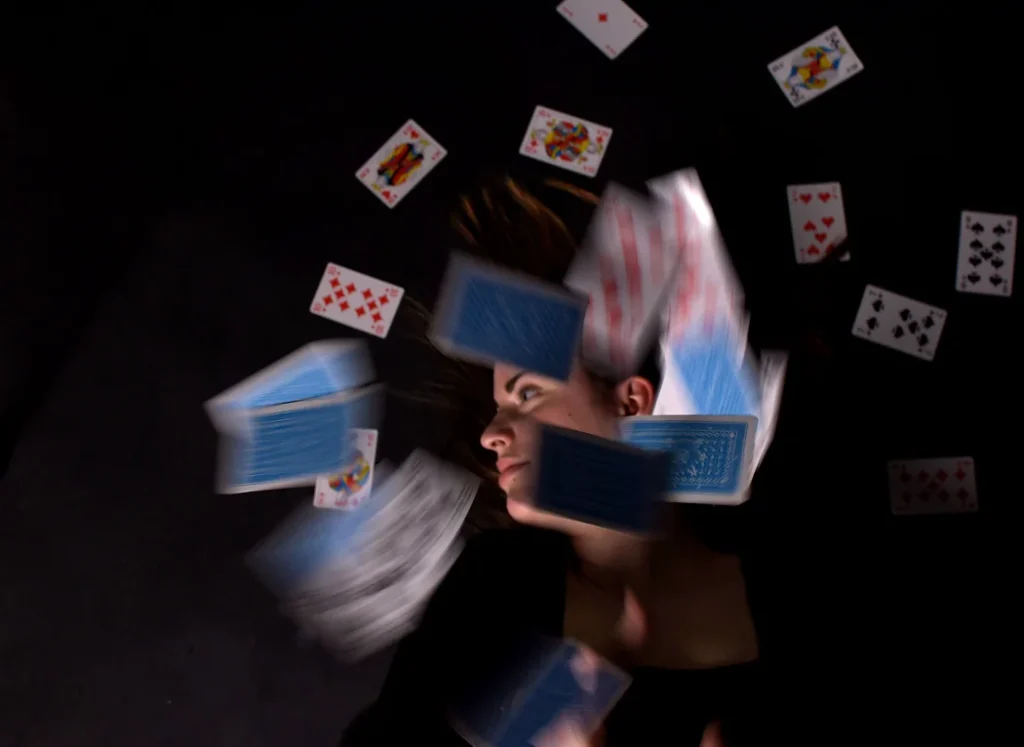 Photo prise d'en haut. Au premier plan des cartes de jeu comme suspendues dans l'air. Au second plan le visage d'une femme blanche de profil.