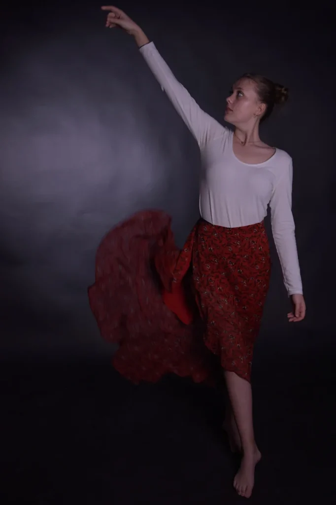 Photo d'une jeune femme blonde. Fond noir. Elle effectue un mouvement de danse.